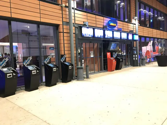 The image shows a large room filled with lots of televisions on the wall, glass windows, lights,...