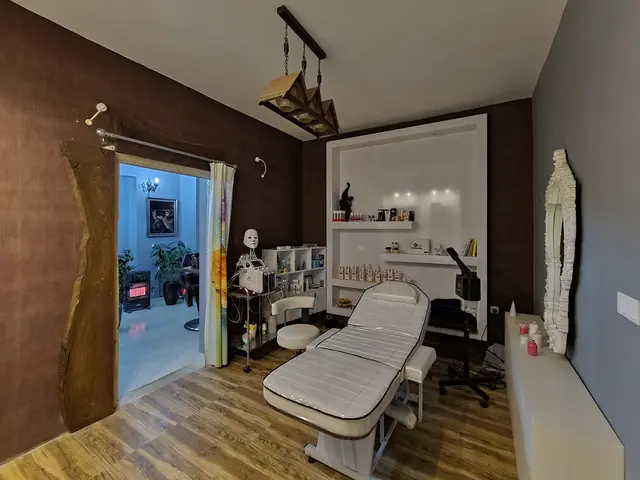 The image shows a room with a massage table and chairs in it, a mirror on the right side, bottles...