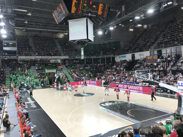 The image shows a basketball game being played in a large arena with a crowd of people watching....