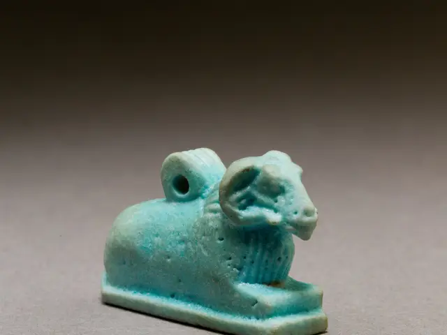 The image shows an ancient Egyptian faience amulet of a ram, which is blue in color and is placed...