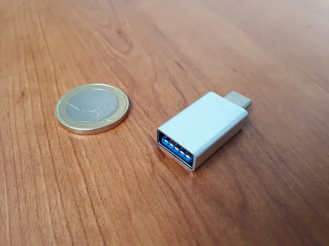 The image shows a USB-C to Type-C adapter sitting on top of a wooden table, with a coin beside it.