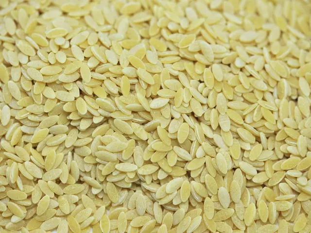 The image shows a pile of yellow flax seeds on a white background. The seeds are a bright yellow...