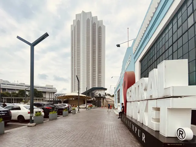 The image shows a bustling central market in Kuala Lumpur, Malaysia, with tall buildings, street...