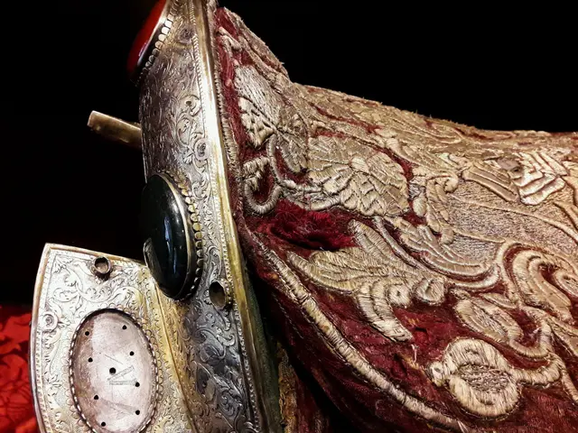The image shows a close up of a horse saddle with a red cloth draped over it. The saddle is adorned...