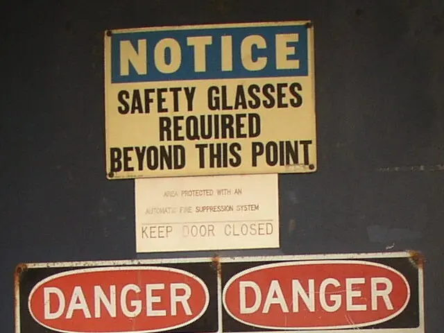 The image shows a notice board with three warning signs attached to the wall. The signs are...