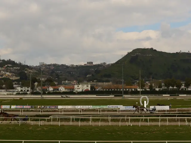 The image shows a horse race track with horses and jockeys on it, surrounded by lush green grass,...