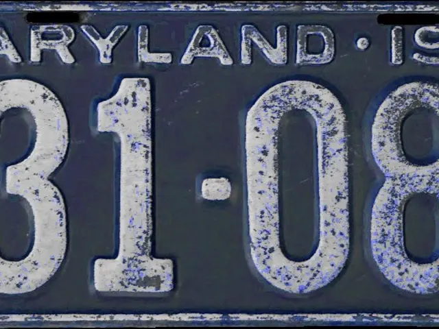 The image shows a blue and white Maryland license plate with the number "1927" written on it...