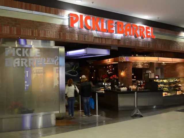 The image shows a pickle barrel restaurant in the middle of a mall, with a group of people standing...