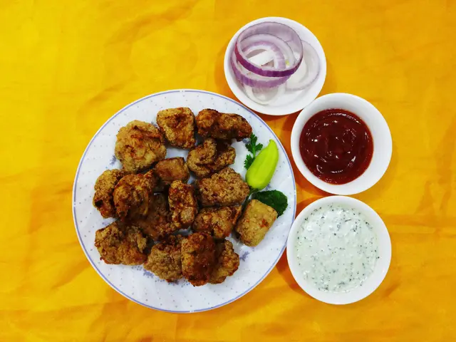 The image shows a white plate topped with fried chicken nuggets and onions, accompanied by two...