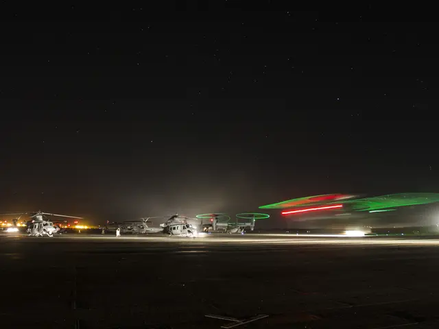 The image shows a group of military helicopters sitting on top of an airport tarmac at night,...