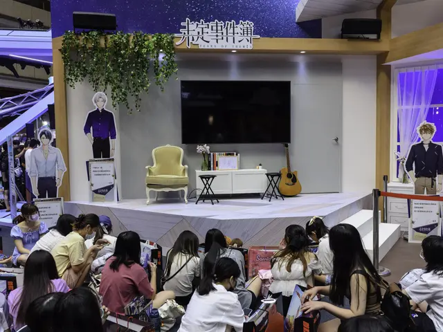 The image shows a group of people sitting on the floor in front of a stage, which is decorated with...