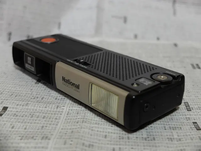 The image shows a black and cream colored radio sitting on top of a newspaper. The radio has a...