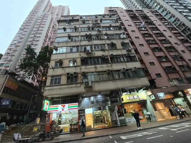 The image shows a bustling city street with tall buildings in the background. There are people...