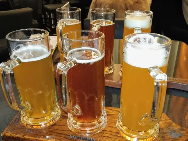 The image shows a wooden tray with four mugs of beer sitting on top of it. In the background, there...